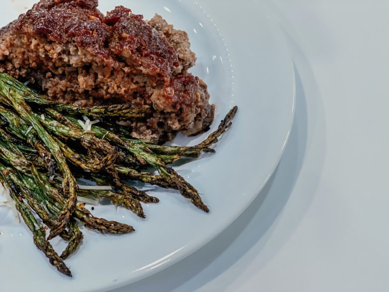 Meatloaf on a white plate with asparagus. 