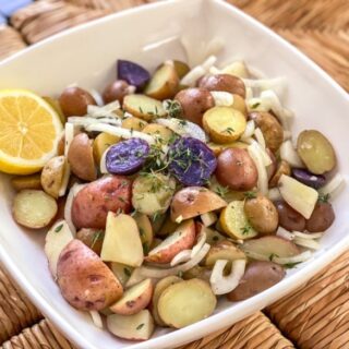 Lemon and thyme potato salad in a bowl with fresh lemon wedges.